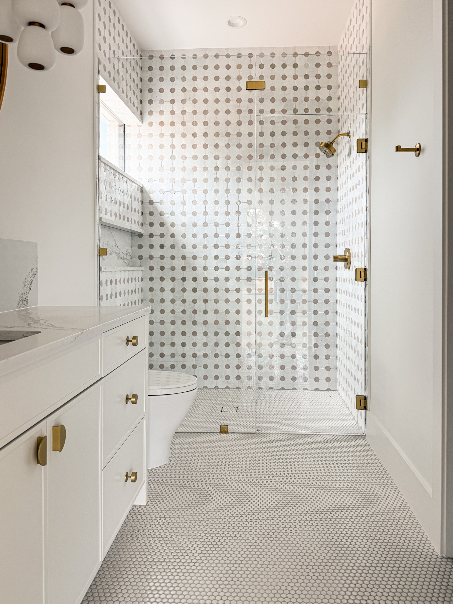 Finished full-frame phone photograph of a bright bathroom with patterned tile and brass fixtures